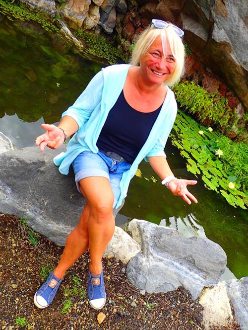 Iris sitzt lachend an einem Teich im Botanischen Garten auf La Gomera